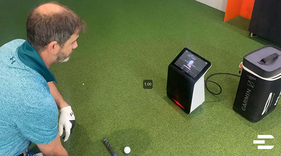 Golfer aligning shot with Garmin Approach R50, highlighting its small hitting zone and built-in screen feedback on indoor turf.