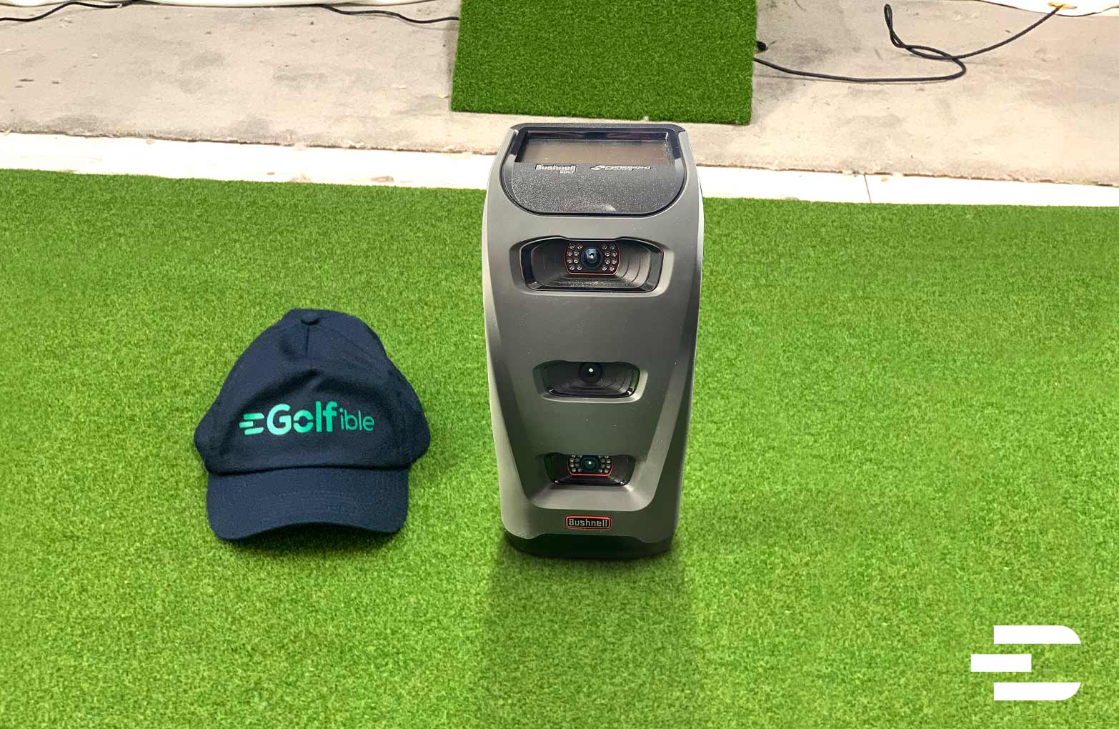 Bushnell Launch Pro front view with Golfible hat on green turf mat in indoor golf studio