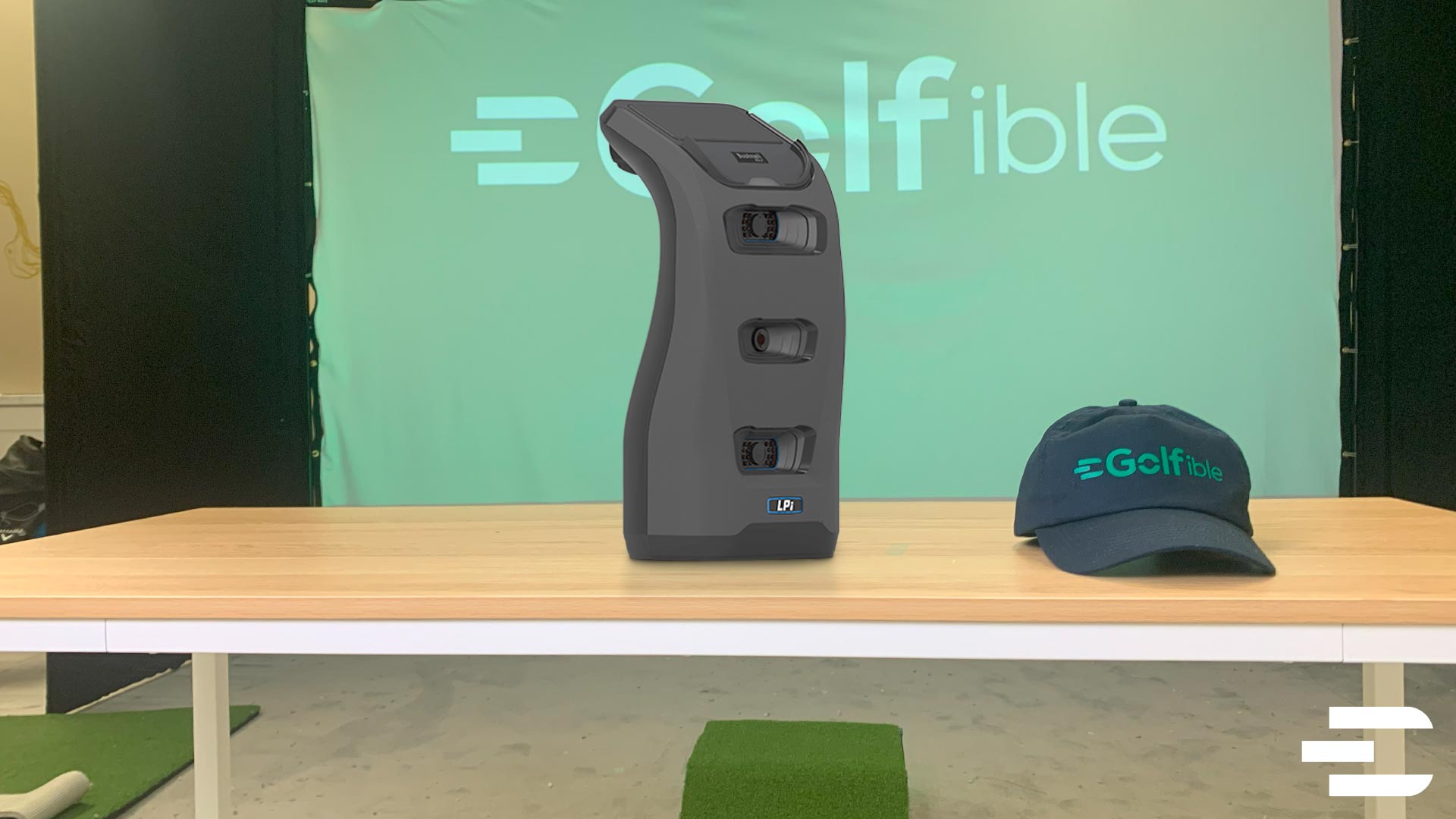 Bushnell LPi launch monitor on table with Golfible hat and branded backdrop in indoor golf studio