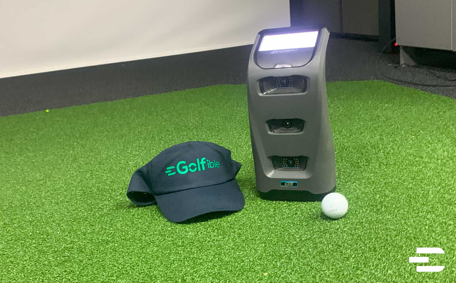Foresight GC3 launch monitor close-up with golf ball and Golfible hat on indoor turf