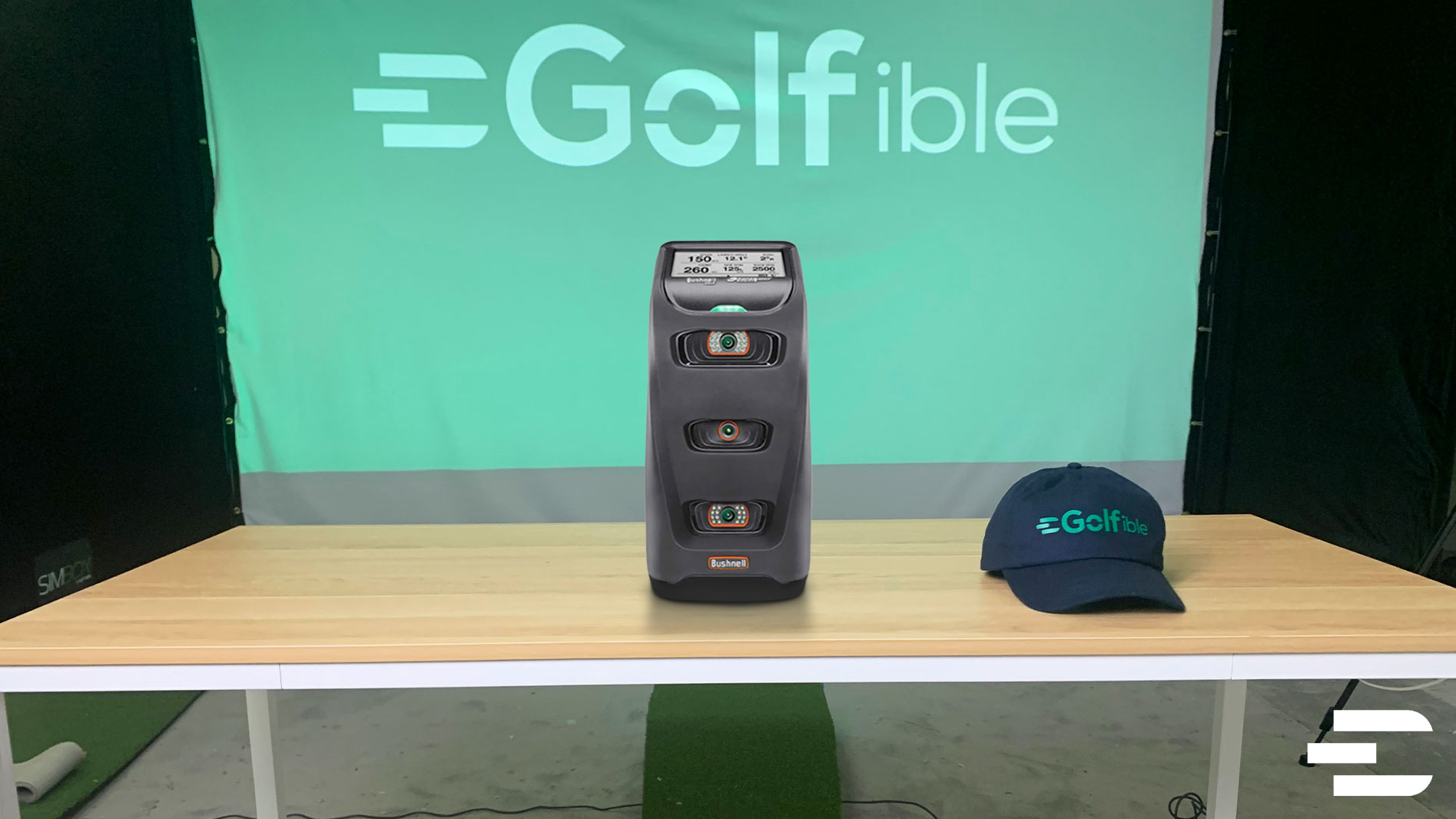 Bushnell Launch Pro golf launch monitor on table with Golfible cap, showing front view of display and camera layout.